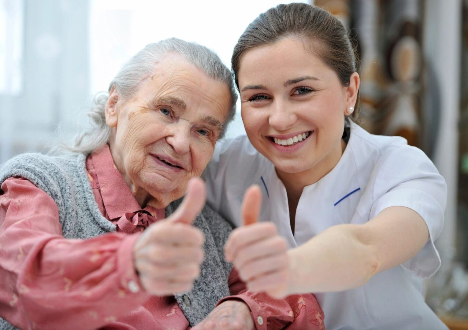 Elderly woman and caregiver smiling with thumbs up.