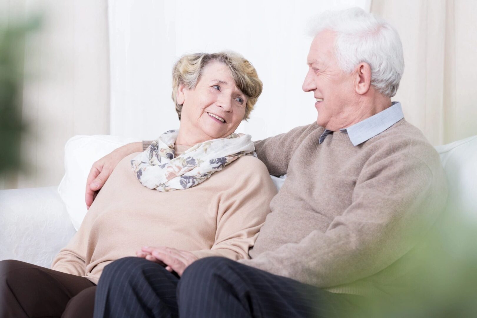 Elderly couple smiling and sitting closely on a couch.