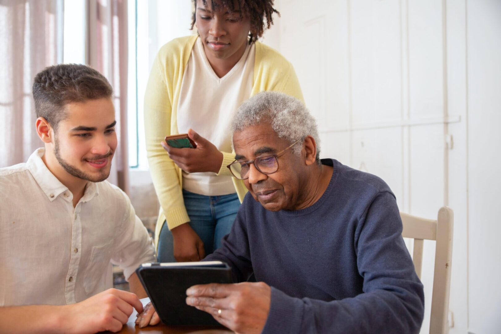 Three people engaging with a tablet, sharing a moment of learning or entertainment.