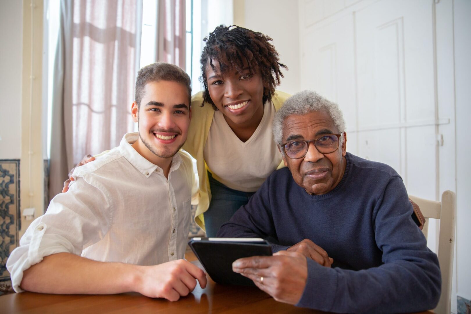 Three generations of men smiling and using a tablet together.