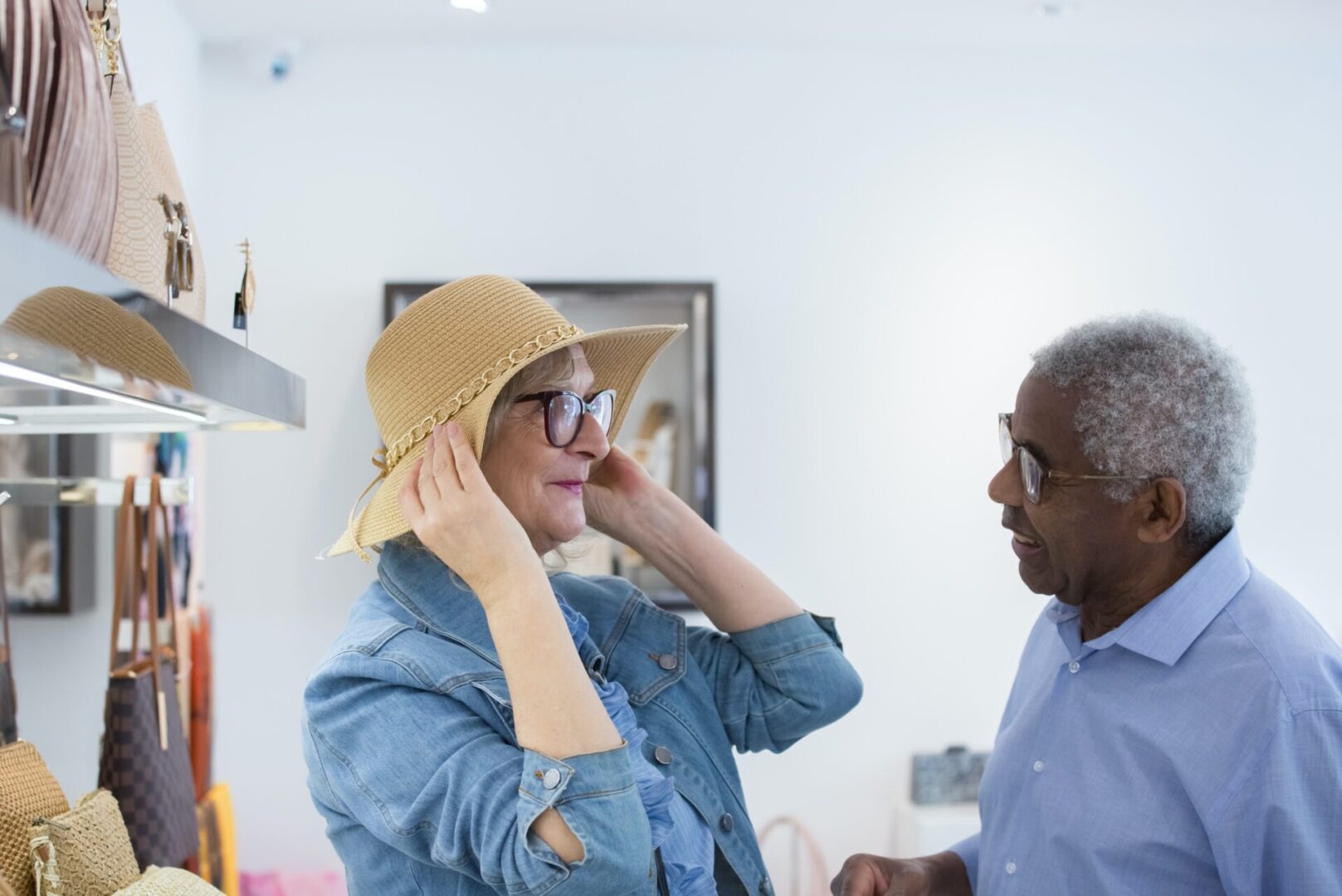 Older man helps woman try on a hat indoors.